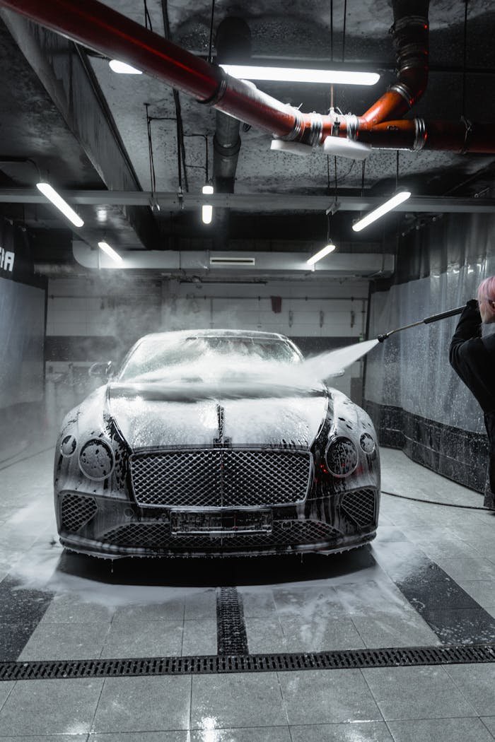 A Bentley Continental GT being washed with foam and a high-pressure hose in a car wash.