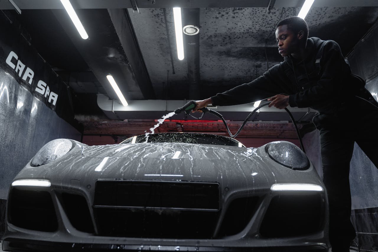 African American man cleaning a white sports car at an indoor car wash. Low angle perspective.